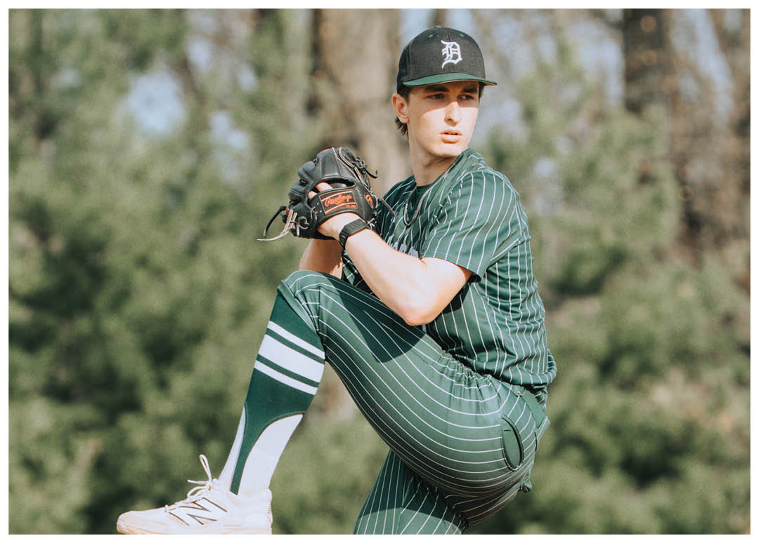 A baseball player wearing a green and white uniform is in the process of throwing a ball. Description generated by AI