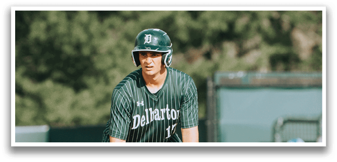 A baseball player in a green and white uniform is crouched down on the field. Description generated by AI