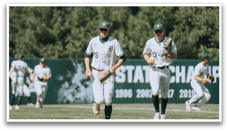 A baseball field with a green wall and a group of men playing baseball. Description generated by AI