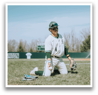 A baseball player kneeling on the grass with a baseball glove. Description generated by AI