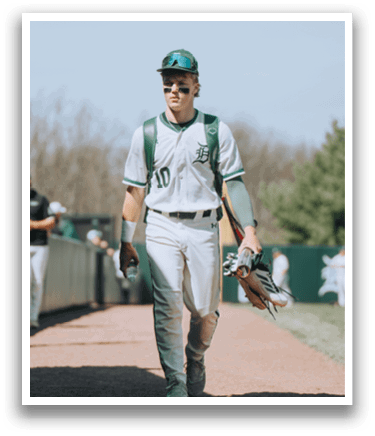 A baseball player wearing a green and white uniform walks down a path. Description generated by AI