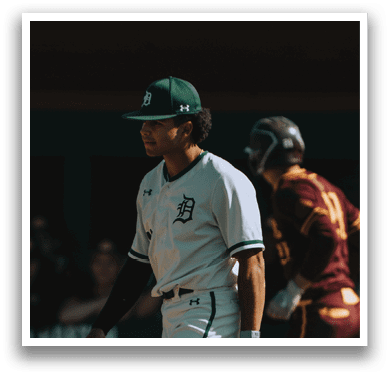 A baseball player wearing a green and white uniform walks on the field. Description generated by AI