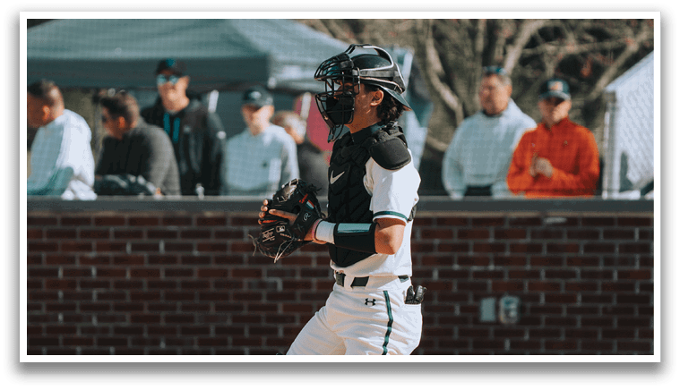A baseball player wearing a green and white uniform is kneeling on the ground. Description generated by AI