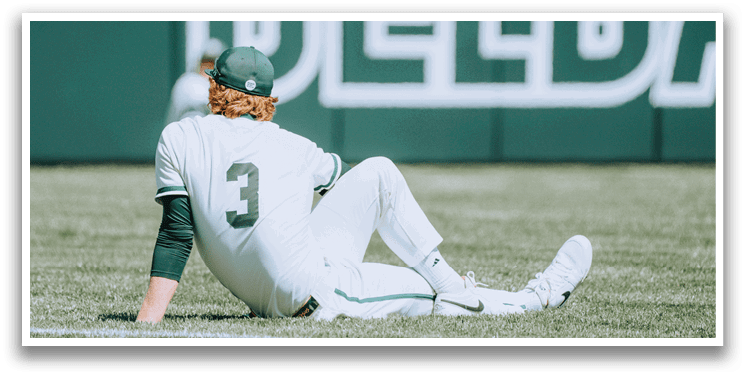 A baseball player wearing a white uniform with the number 3 on it is sitting on the grass. Description generated by AI