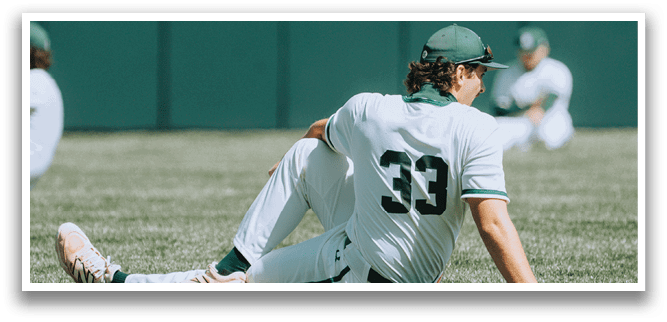 A baseball player wearing a green hat and white uniform is sitting on the grass. Description generated by AI