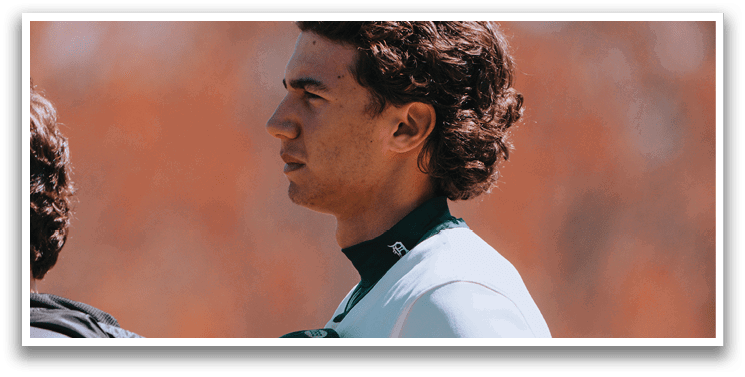 A man wearing a baseball uniform with a green and white shirt and a black hat. Description generated by AI