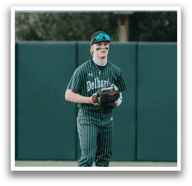 A baseball player wearing a green and white uniform stands on a baseball field. Description generated by AI