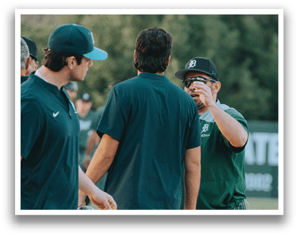A group of men wearing green and white shirts are standing on a baseball field. Description generated by AI