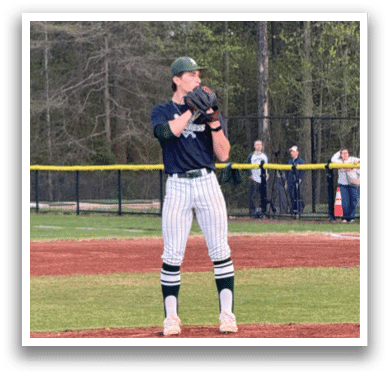 A baseball player in a blue shirt and green hat stands on a mound. Description generated by AI