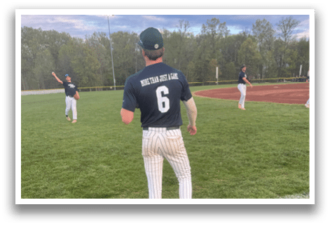 A baseball player wearing a blue shirt and white pants stands on a field. Description generated by AI