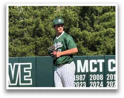 A baseball player in a green shirt and white pants is standing on the pitcher's mound. Description generated by AI