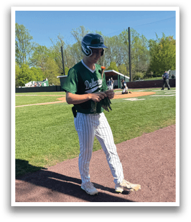 A baseball player wearing a green and white uniform walks on the field. Description generated by AI