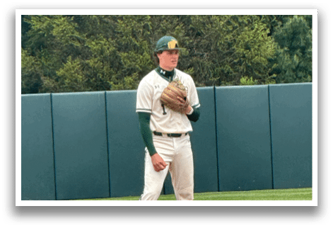 A baseball player in a white uniform and green sleeves is standing on a baseball field. Description generated by AI