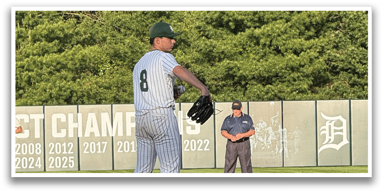 A baseball player in a green and white uniform is standing on the pitcher's mound. Description generated by AI