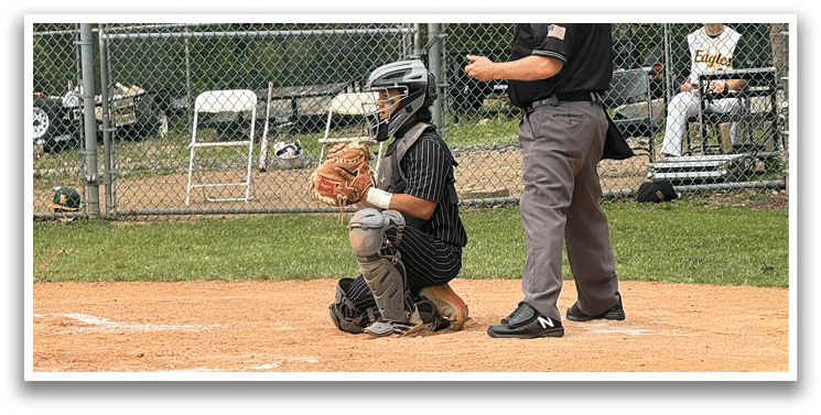 A baseball game is taking place with a man in a black shirt and gray pants standing behind a catcher. Description generated by AI