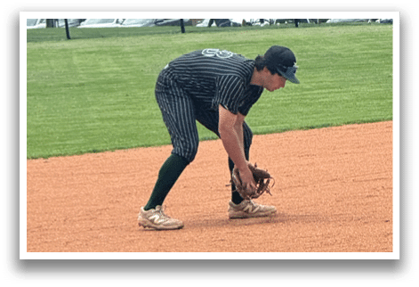A baseball player in a black shirt and black socks is bending over to catch a ball. Description generated by AI
