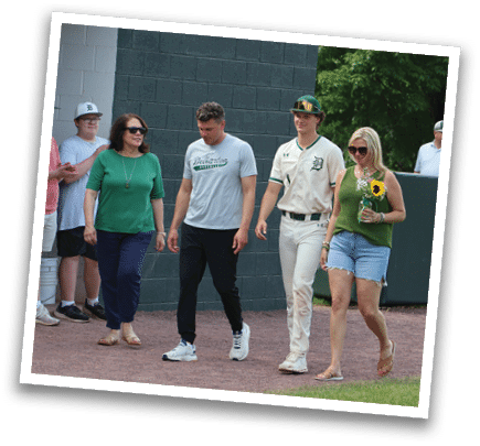 A group of people standing in front of a baseball field. Description generated by AI