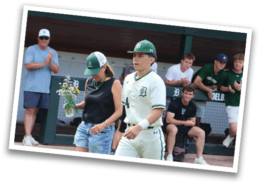 A man wearing a green hat and white uniform walks on a baseball field. Description generated by AI
