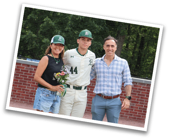 A man, woman, and boy are standing in front of a baseball field. Description generated by AI