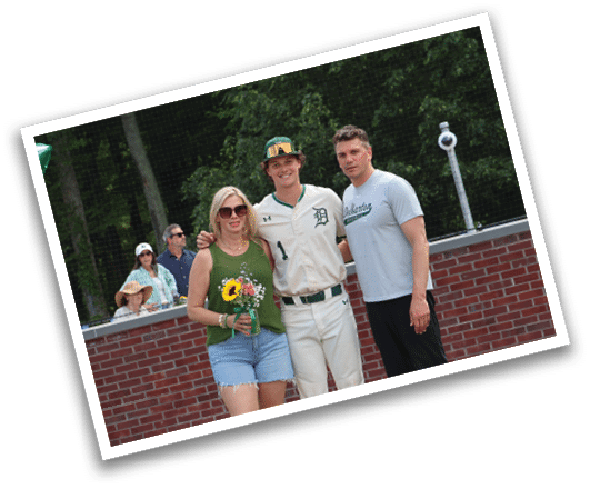 A man and woman are standing in front of a baseball field. Description generated by AI