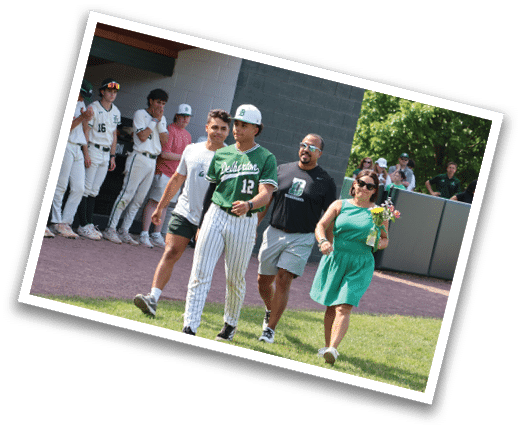 A man wearing a green shirt and white pants walks with a woman in a green dress. Description generated by AI