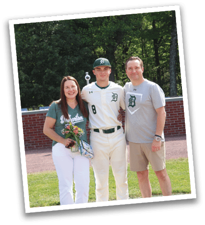 A man and woman are standing in front of a baseball field with a baseball player in a white uniform. Description generated by AI