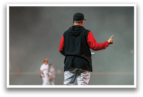 A man wearing a black and red jacket stands on a baseball field, pointing at a player. AI generated content