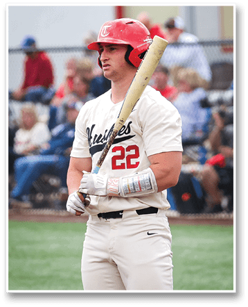 A baseball player wearing a red helmet and a white jersey with the number 22 on it. He is holding a baseball bat and standing on a field. AI generated content