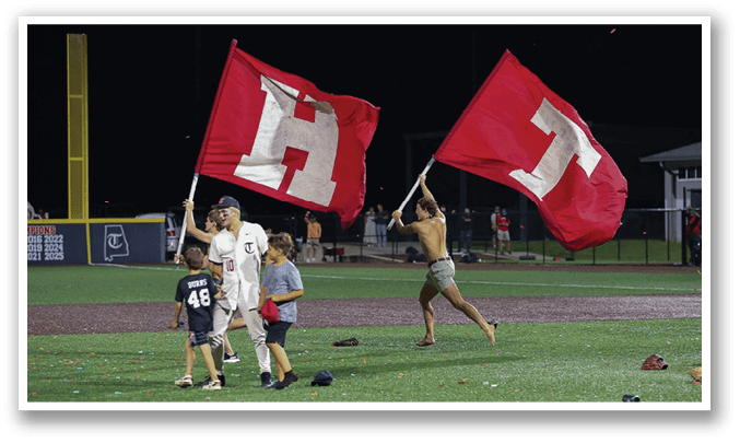 A group of people are standing on a baseball field, holding up red and white flags. AI generated content