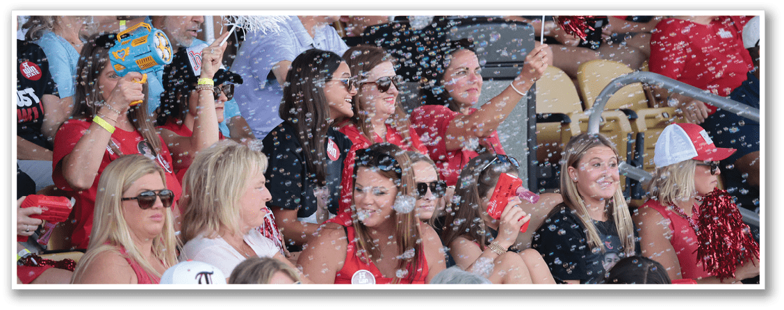 A group of people are sitting in the stands at a sporting event, watching the game. They are enjoying the event and having a good time. AI generated content