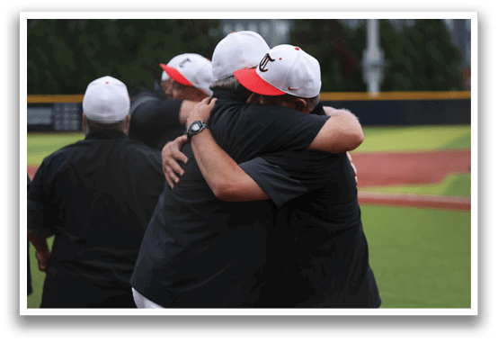 Two men wearing baseball caps and black shirts hugging each other on a baseball field. AI generated content