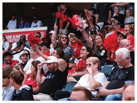 A group of people are sitting in the stands at a baseball game, with some of them holding up red and white pom poms. AI generated content