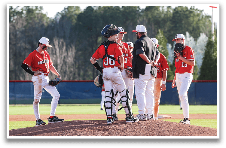 A group of baseball players on a field, some of them wearing red shirts, standing around and talking. AI generated content