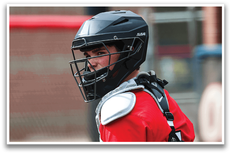 A young boy wearing a baseball helmet and catcher's gear is sitting on the ground. AI generated content