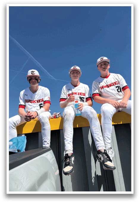 Three young men wearing baseball uniforms are sitting on a ledge. AI generated content