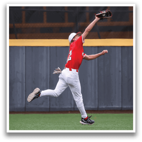 A baseball player in a red shirt and white pants is leaping in the air to catch a ball. AI generated content