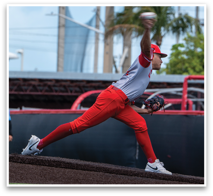 A baseball player in a red and grey uniform is pitching a ball. Description generated by AI