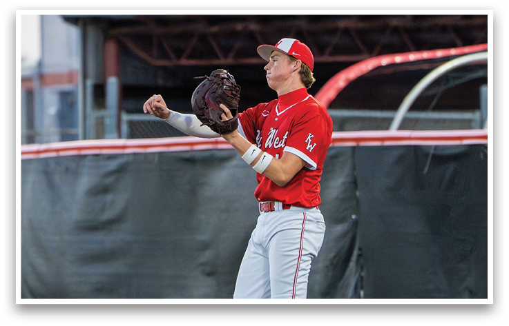 A baseball player wearing a red shirt and white pants is holding a baseball glove. Description generated by AI