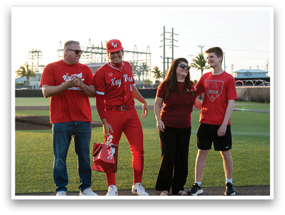 A man in a red baseball uniform is standing next to a woman and a boy. Description generated by AI