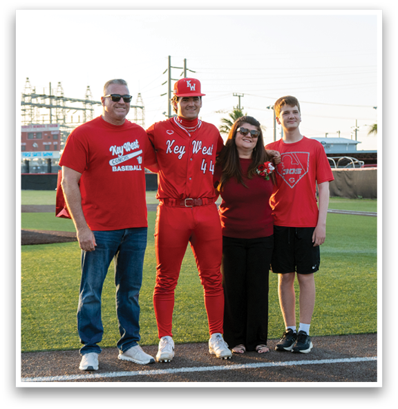 A man and woman in red shirts stand on a baseball field with a man in a red shirt and red pants. Description generated by AI
