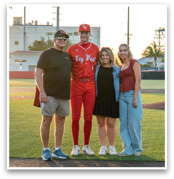A man in a red baseball uniform stands between a man and a woman. Description generated by AI
