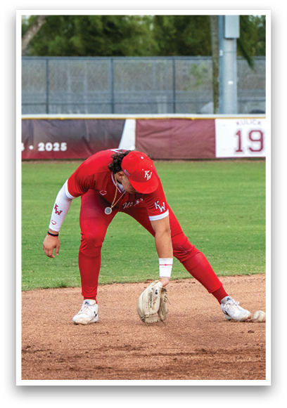 A baseball player wearing a red jersey and red pants bends over to catch a ball. Description generated by AI