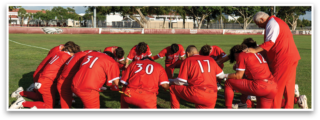 A group of people wearing red shirts and red pants are kneeling on the grass. Description generated by AI