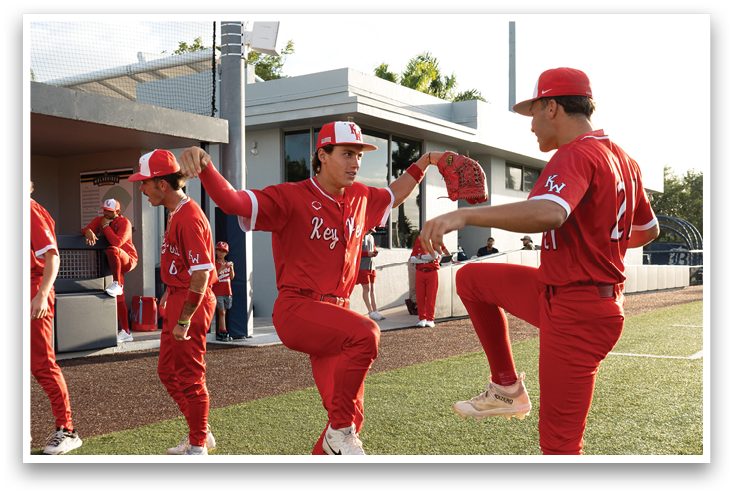 A group of men in red shirts are practicing baseball on a field. Description generated by AI