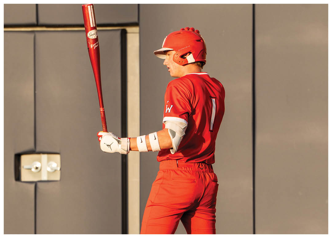 A baseball player in a red jersey holding a bat. Description generated by AI