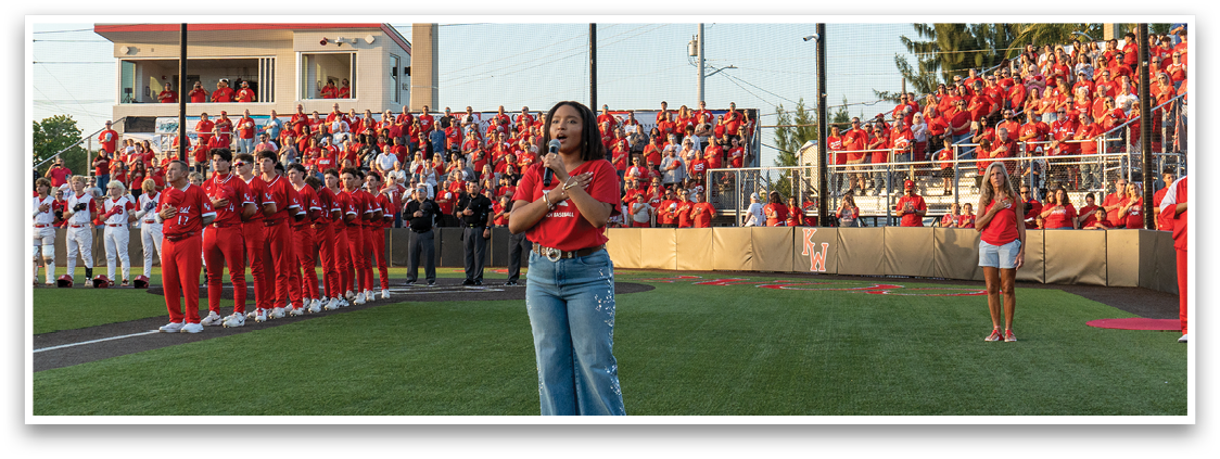 A woman in a red shirt stands on a field. Description generated by AI