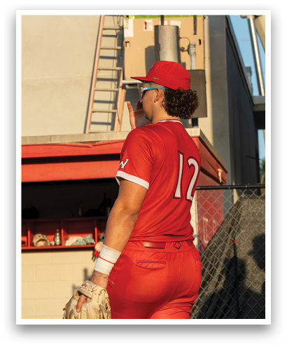 A person wearing a red baseball uniform is standing in front of a flag. Description generated by AI