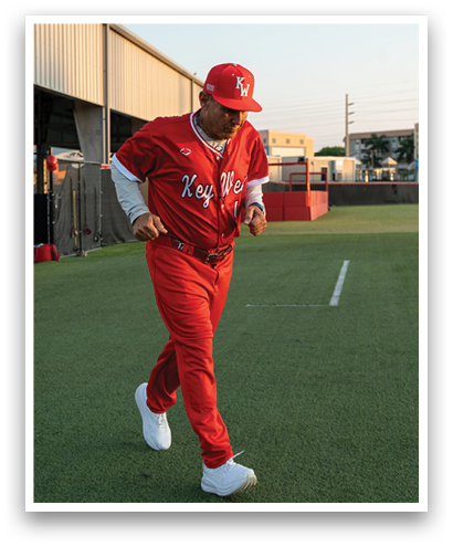 A man wearing a red baseball uniform is walking on a grassy field. Description generated by AI