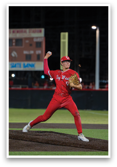 A baseball player in a red jersey and red pants is pitching a ball. Description generated by AI
