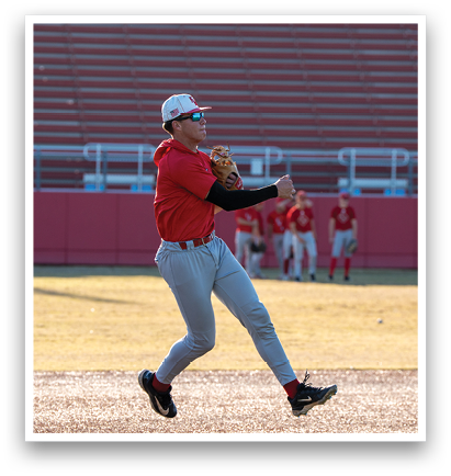 A baseball player in a red shirt and grey pants is leaping in the air to catch a ball. AI generated content